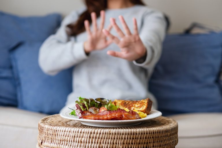 A woman making hand sign to refuse food on the table for dieting and healthy eating concept