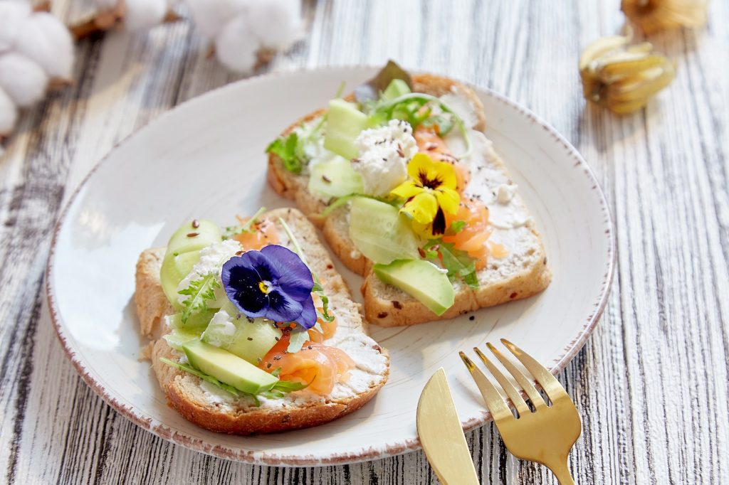 Aesthetic toasts with smoked salmon, avocado, cucumber and edible flowers. Pescetarian diet.