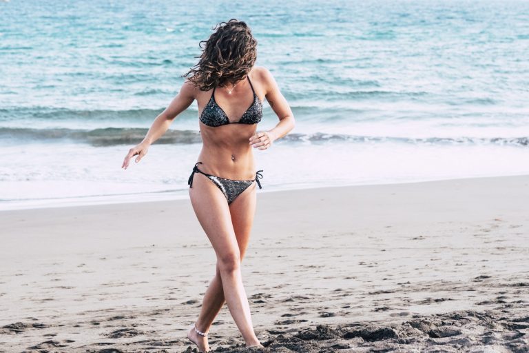 Beautiful young woman in bikini walking on sand at beach. Young woman enjoying summer