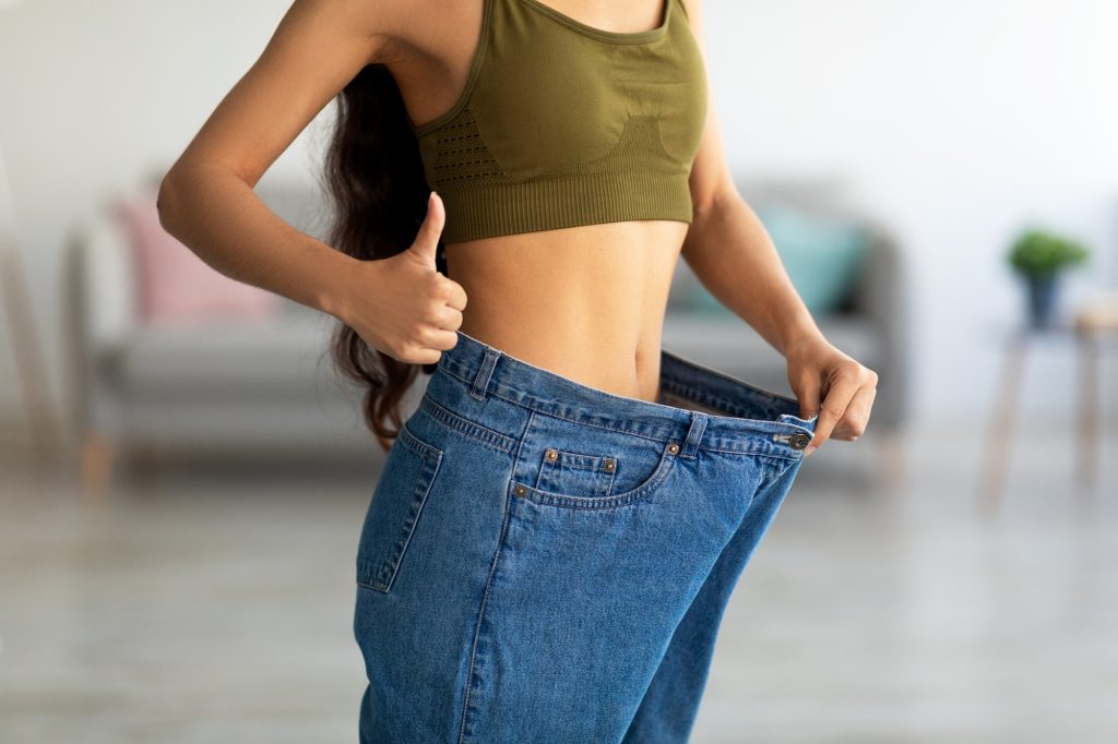 Closeup of young Indian lady in big jeans showing thumb up, recommending her weight loss program