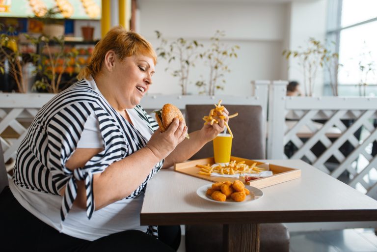 Fat woman eating high calorie food in restaurant