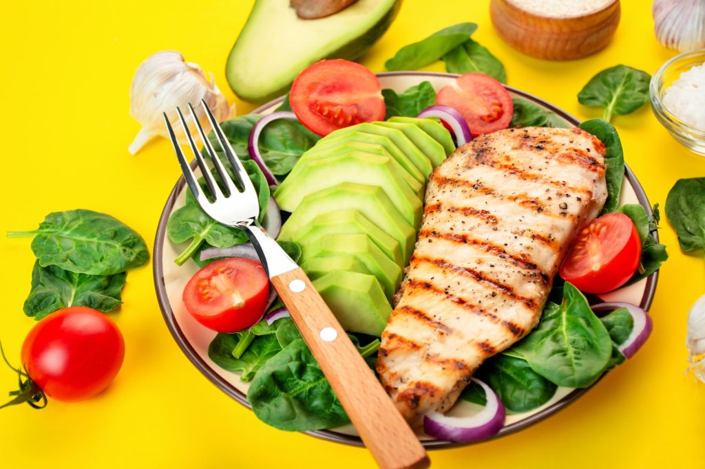 Grilled chicken breast with avocado and herbs on a bright yellow background.Ketogenic diet