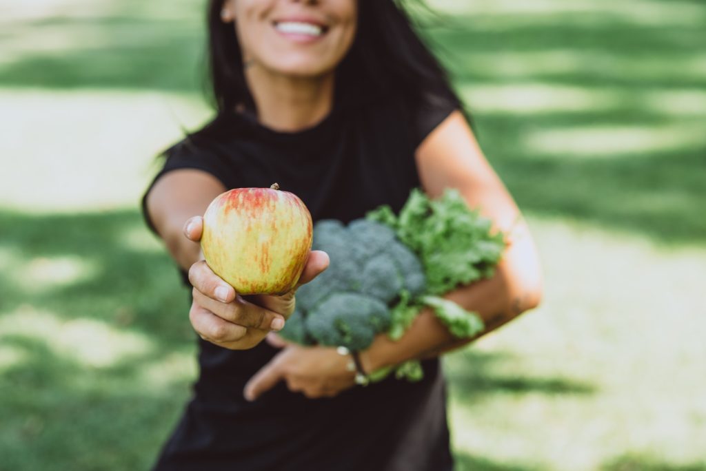 Happy woman holding an apple, broccoli and green salad in her hands. Healthy food, diet.