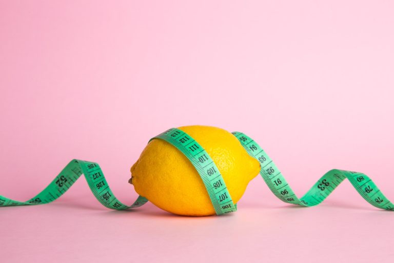 Lemon and tape measure on pink background. Diet concept.