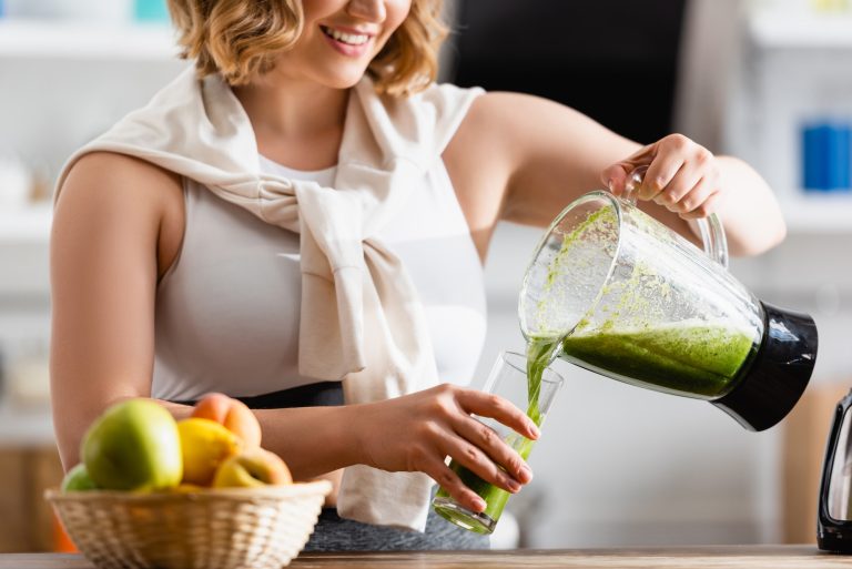 partial view of young woman pouring mixed green smoothie in glass