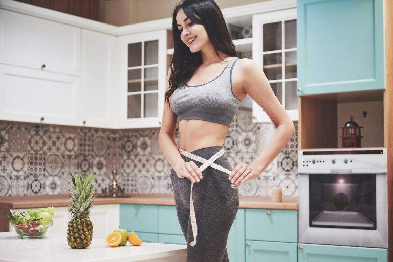 Portrait of a woman measuring her slim body on a kitchen background. Fitness and healthy lifestyle
