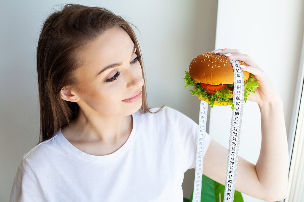 Woman holding harmful fat burger with measuring tape.