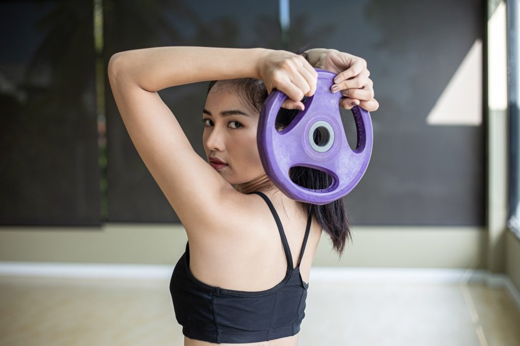 Women exercise with dumbbell weight plates and twist to the back.