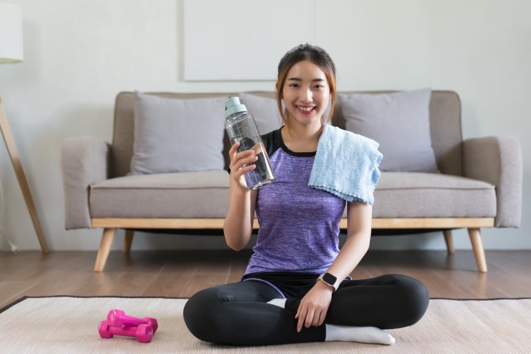 Young asian woman sitting on the floor to relaxing and drinking water after doing exercise at home