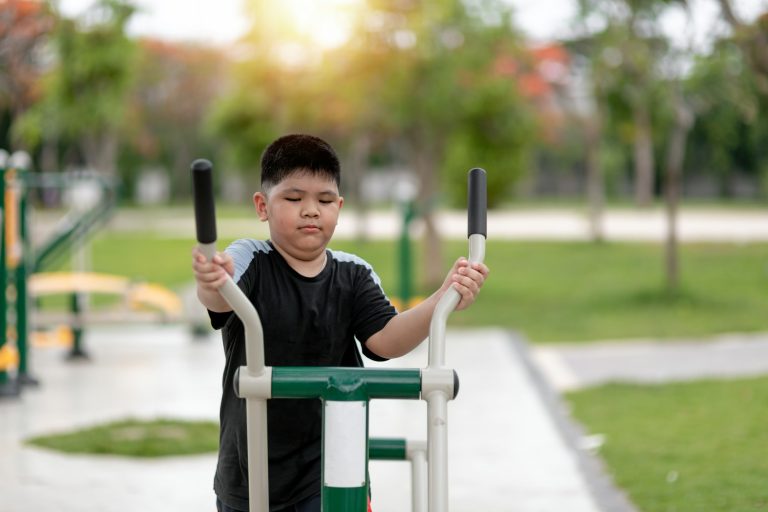 fat boy trains on fitness equipment in the park